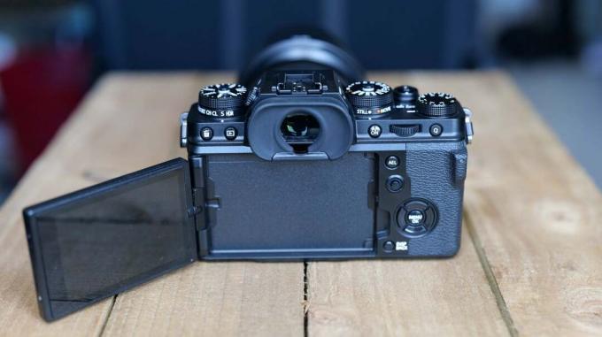 Melnas Fujifilm XT4 kameras sānskats no aizmugures, kas stāv uz koka galda ar atvērtu ekrānu