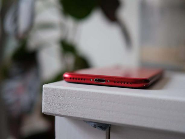 Raudono iPhone SE, padėto aukštyn kojomis ant baltos lentynos, apatinio krašto vaizdas