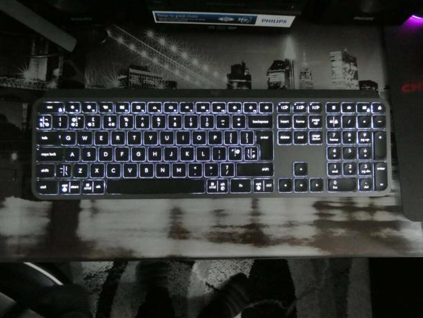 Utsikt fra toppen av et svart Logitech MX-tastatur holdt på et bord med lys under tastene