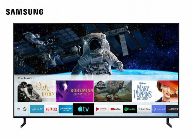 Черен телевизор Samsung, стоящ на бял фон, показващ Apple TV Airplay на началния екран